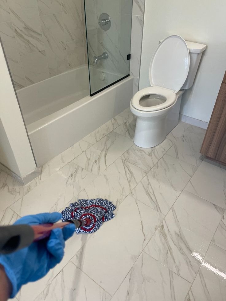 Gloved hand mopping a marble-look bathroom floor beside a tub and toilet