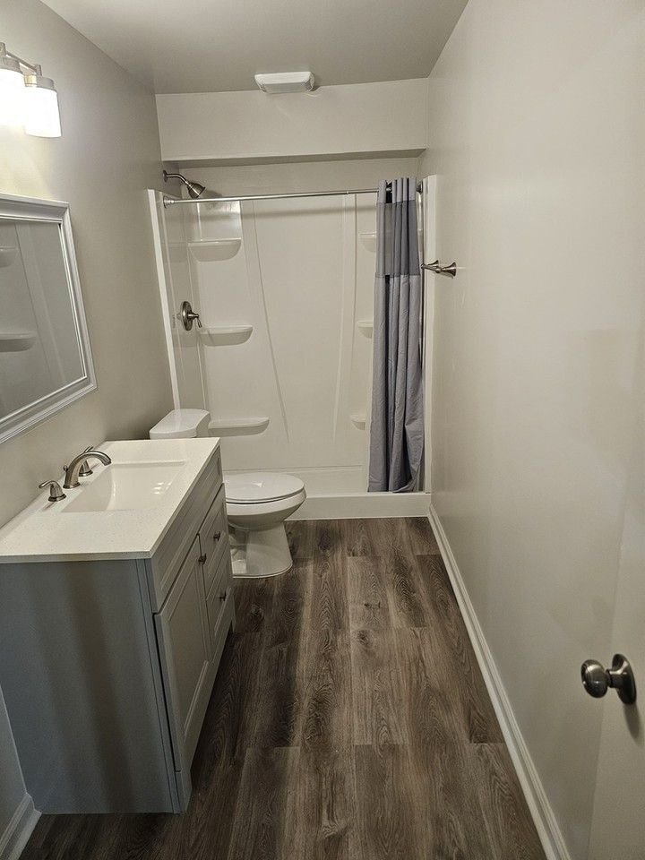 Clean bathroom with a vanity, shower and wood-look floor