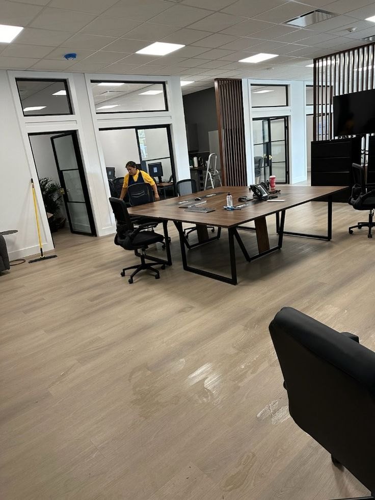 Cleaner tidying around a large conference table in an open office