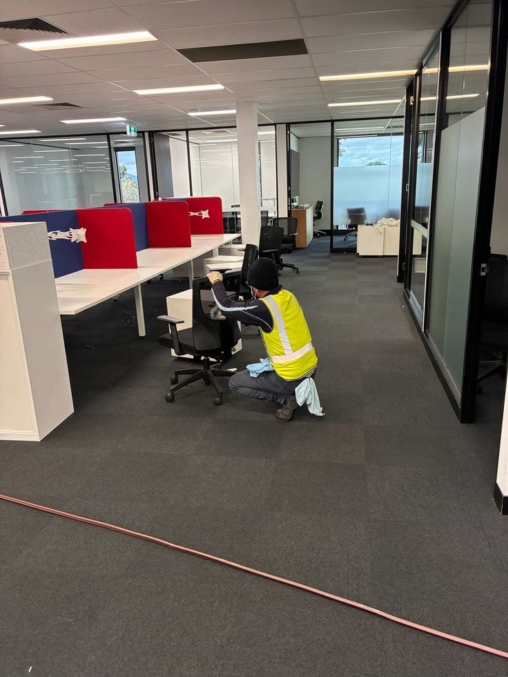 Cleaner in a safety vest wiping an office chair and desks